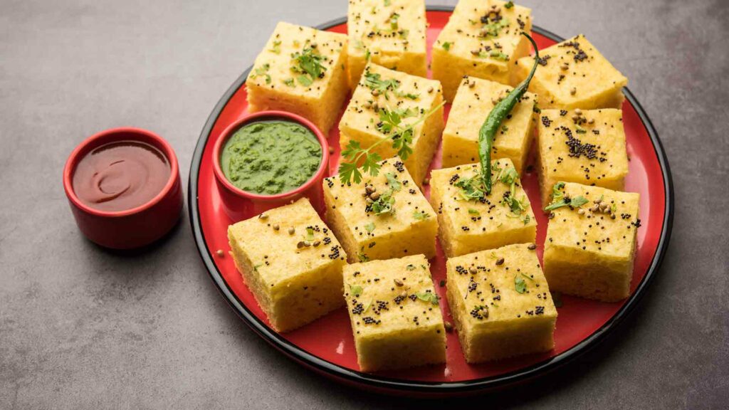 Dhokla (Gujarati Dish) in a red plate with tomato and mint sauce with grey background
