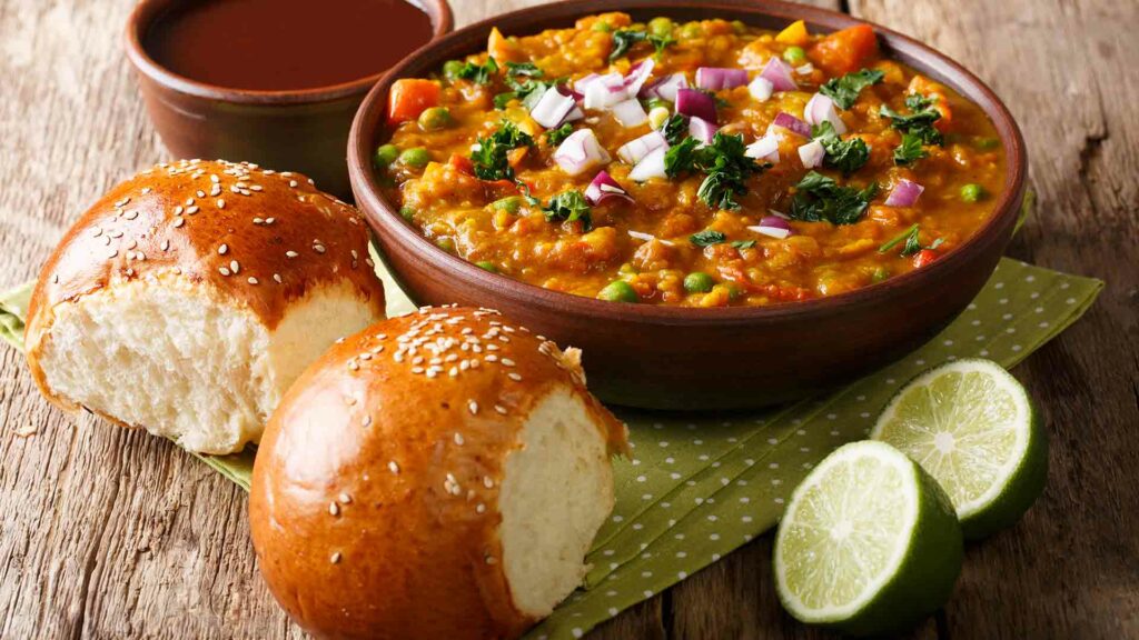Pav Bhaji in a bowl with lime and sauce and placed in a wooden table