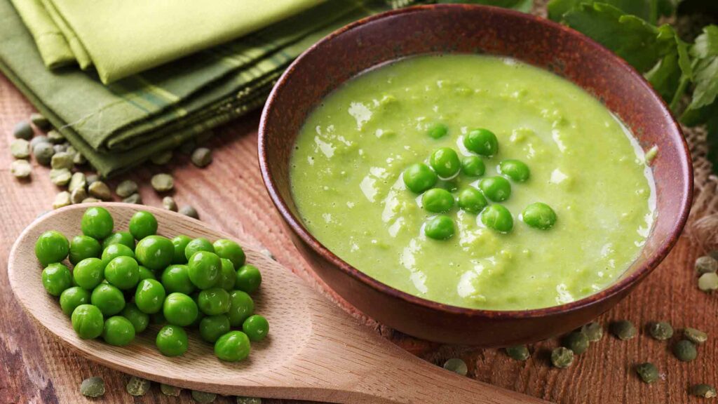 Indian Style Pea Soup in a brown bowl place in a wooden table and a spoon with peas then a green cloth in that table