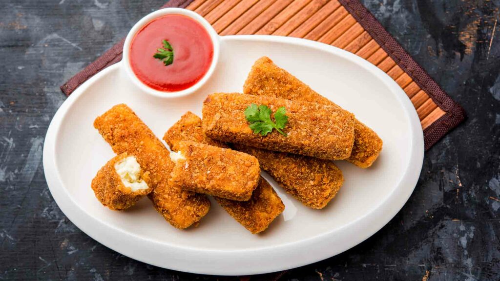 crispy paneer fingers in white oval shaped white plate with tomato sauce