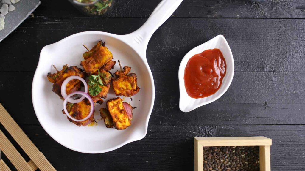 Paneer Tikka in a white pan with tomato sauce near with grey background